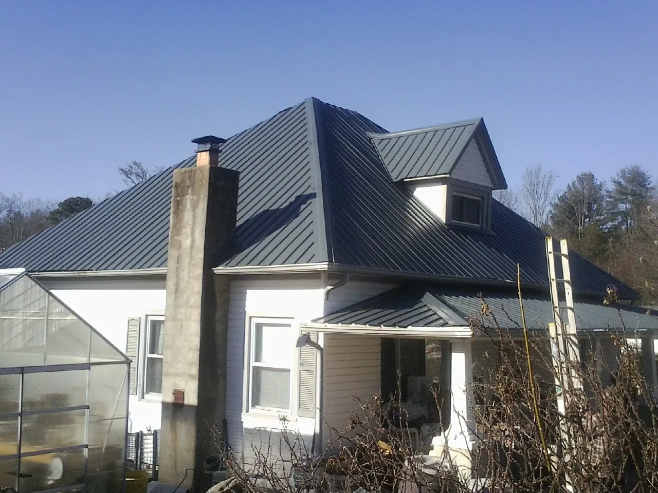Dark blue standing seam metal roof on a white farmhouse with dormer — Slate & Tile Roof Repair by Roofing Brothers in Glen Richey