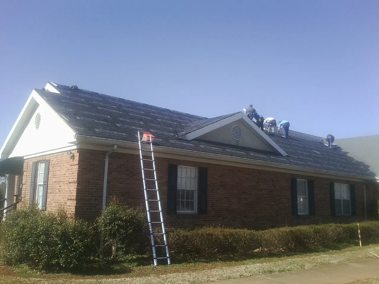 Crew tearing shingles off a brick ranch roof with a ladder set — Emergency Roof Repair work by our crew in Glen Richey