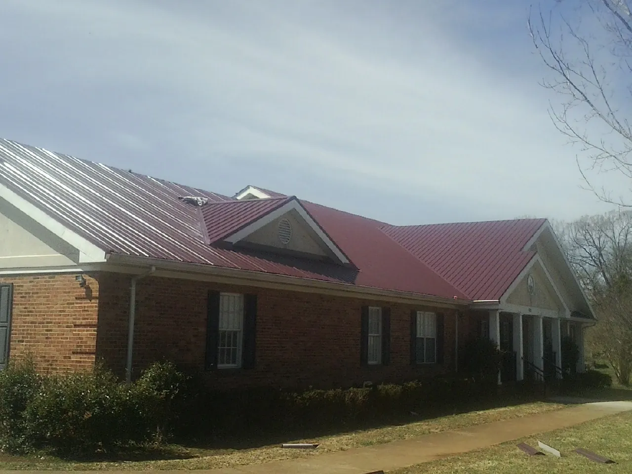 Red metal roof with gabled entries on a long brick building, from a Hail Damage Roof Repair job in Glen Richey