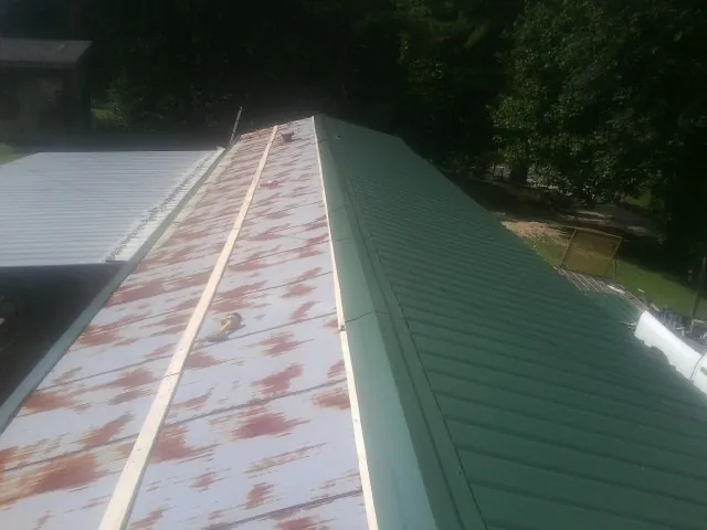 Old rusted panels beside newly installed green metal roofing — Wind Damage Roof Repair by Roofing Brothers in Glen Richey