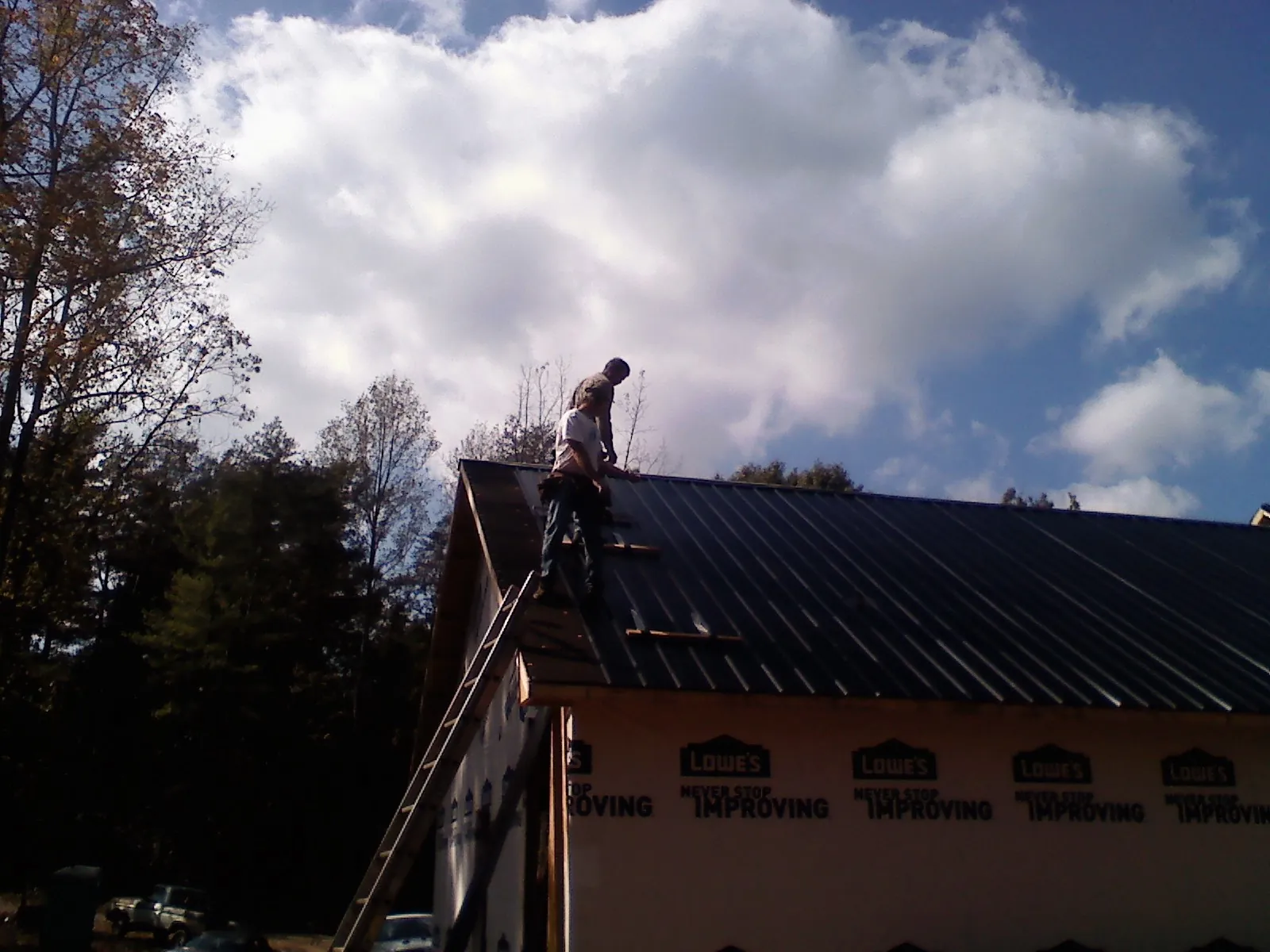 Roofer fastening dark metal panels high against a cloudy sky, from a Roof Inspection job in Glen Richey