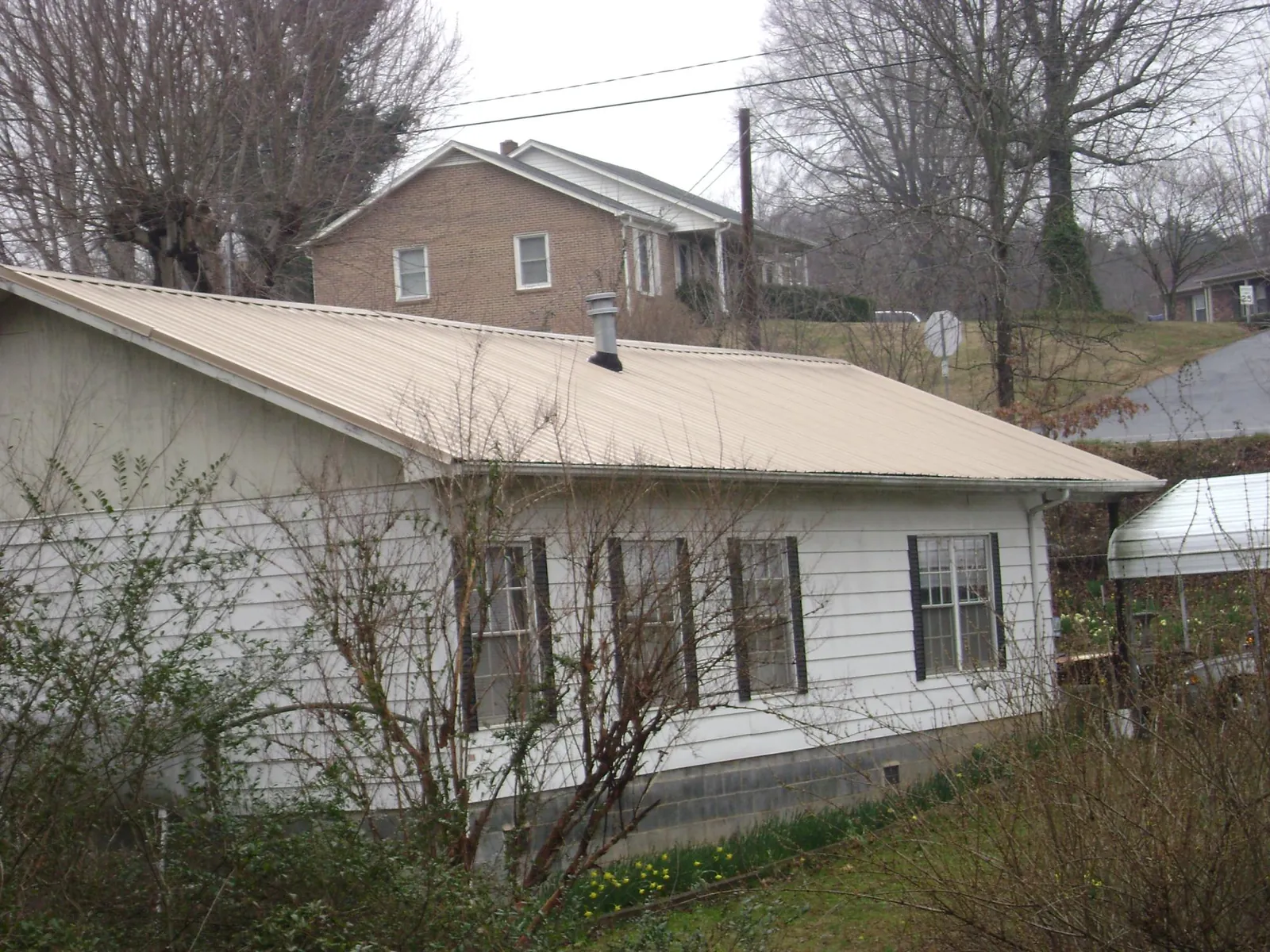 Tan metal roof on a white sided house set into a hillside — Commercial Roofing by Roofing Brothers in Glen Richey